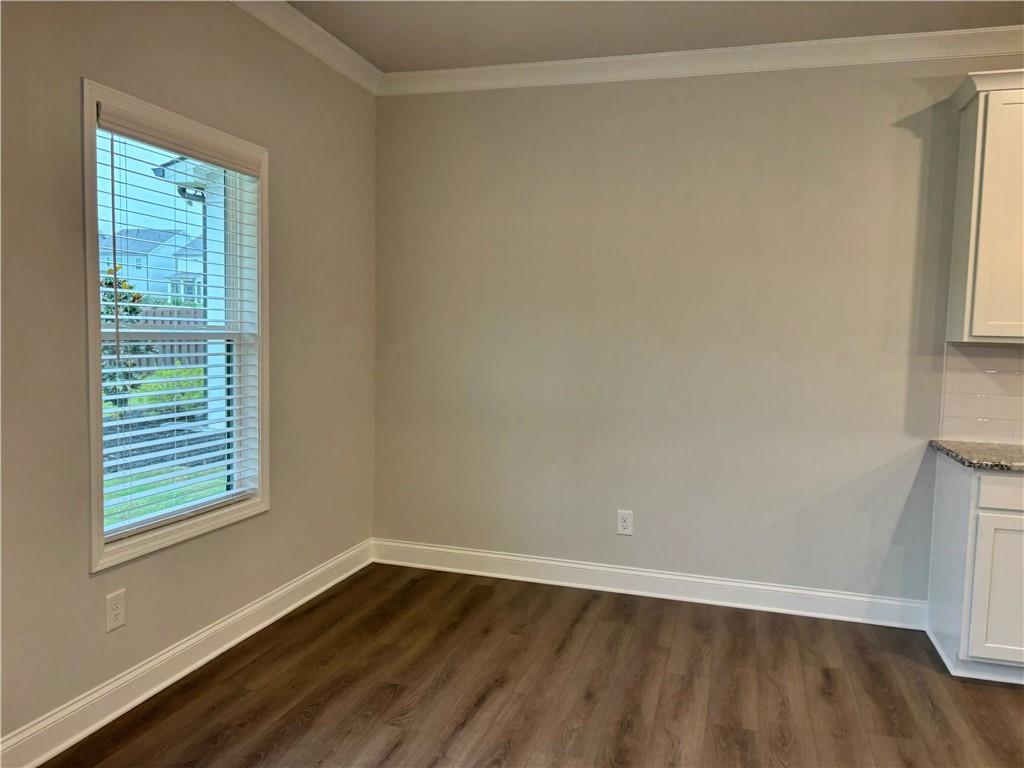 Unfurnished dining area with wood-look flooring, a window with blinds, and partial kitchen cabinetry.