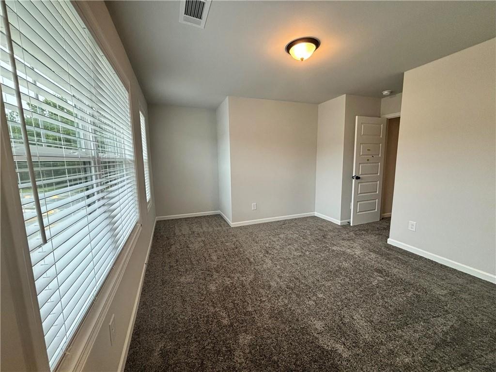 Empty carpeted room with large windows covered by white blinds.
