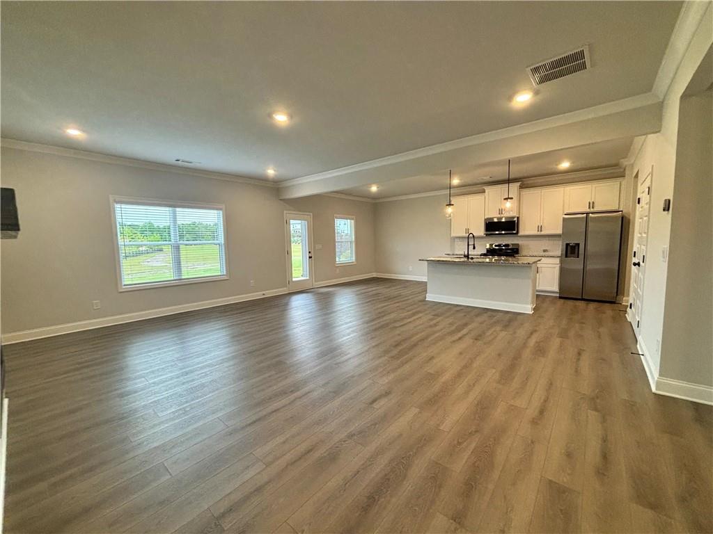 Open living area and kitchen with wood-look floors, white cabinets, and stainless steel appliances.