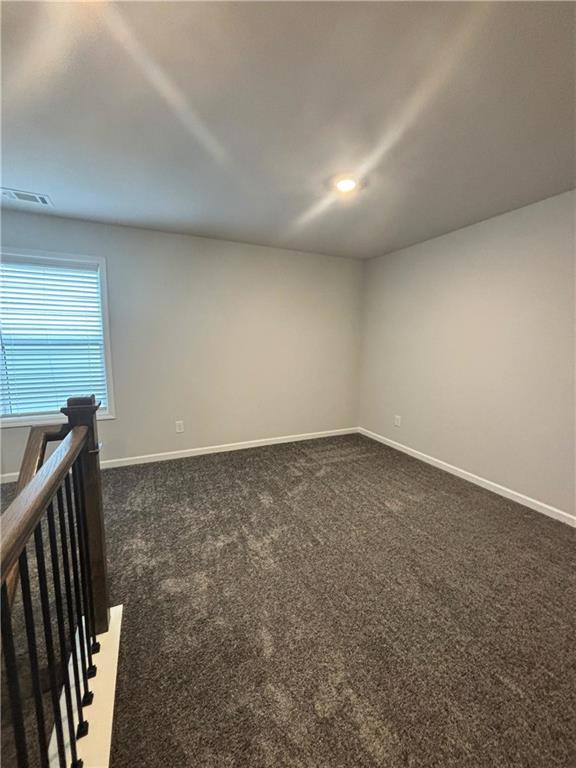 Empty carpeted upstairs room with a window and stair railing.