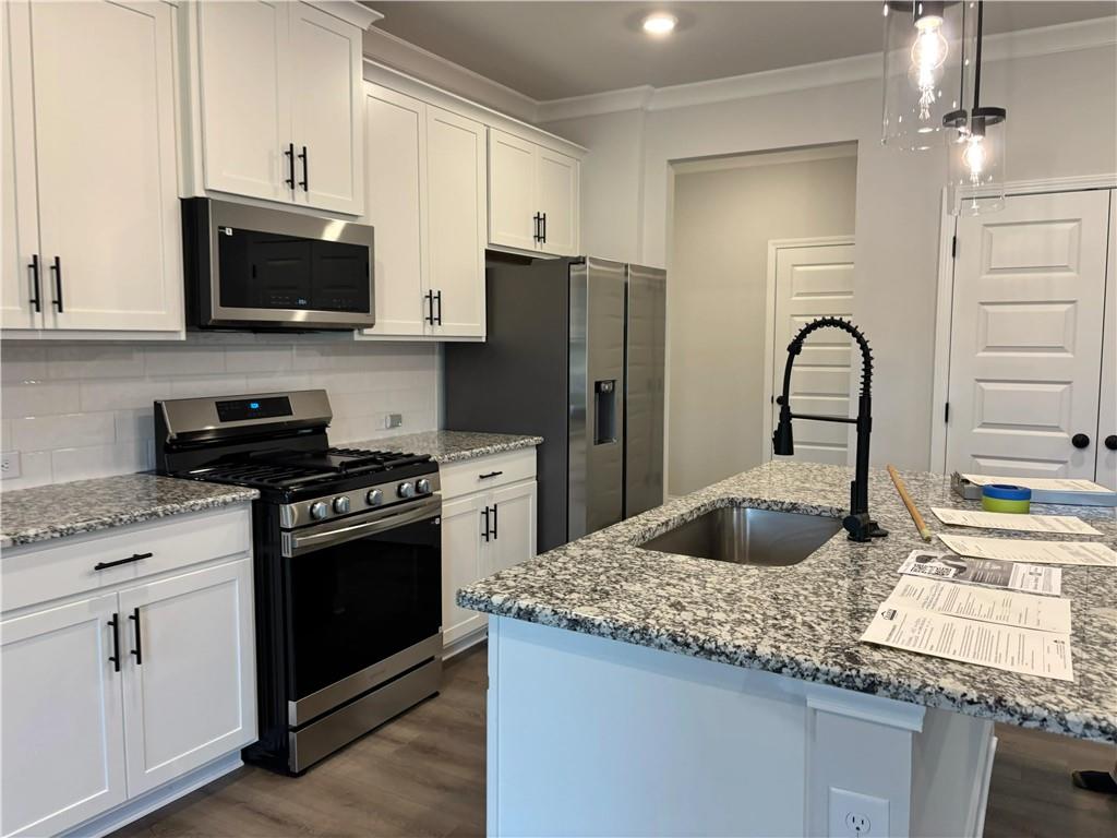 Kitchen with white cabinets, stainless steel appliances, and a granite island with a deep sink.