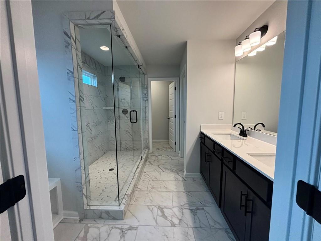 Bathroom with a glass-enclosed marble shower and dark double vanity.