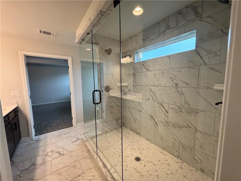 Bathroom with a glass-enclosed walk-in shower lined in marble-look tile and a narrow window.