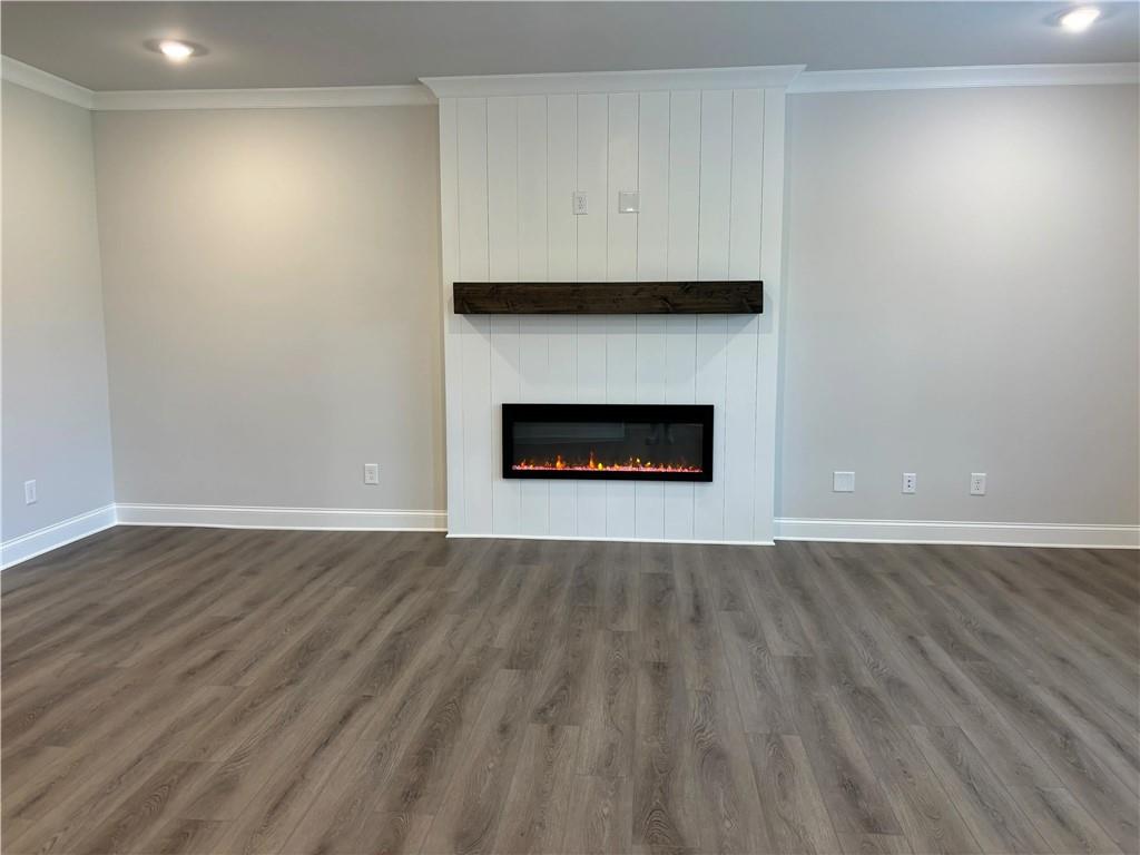 Empty living room with a white paneled fireplace wall, dark wood mantel, and gray wood-look flooring.
