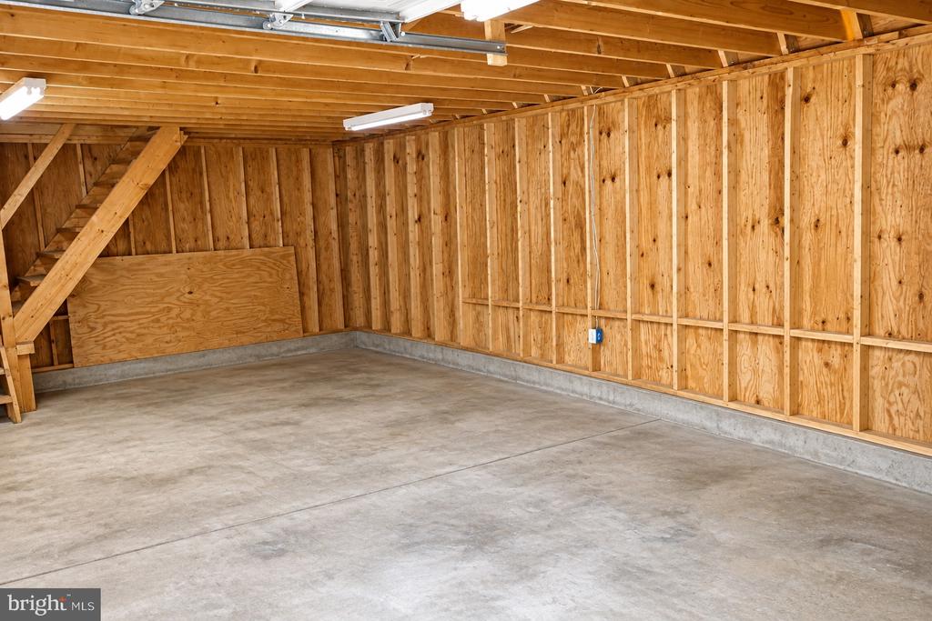 Empty garage with a concrete floor, exposed plywood walls, and overhead door tracks.