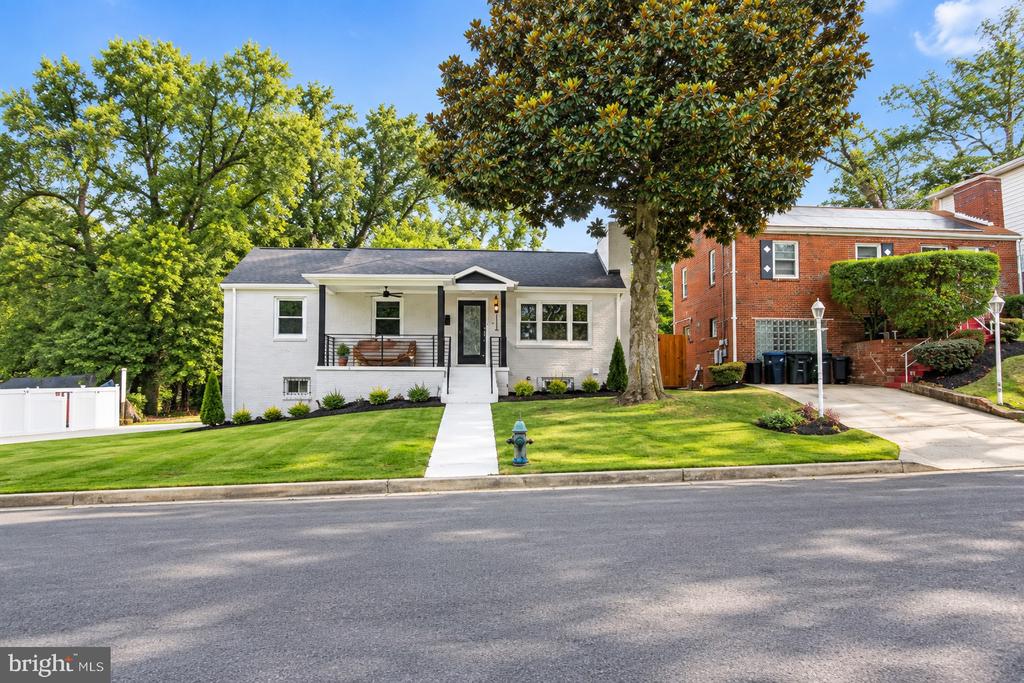White single-story home with a covered porch, landscaped lawn, and large mature tree.