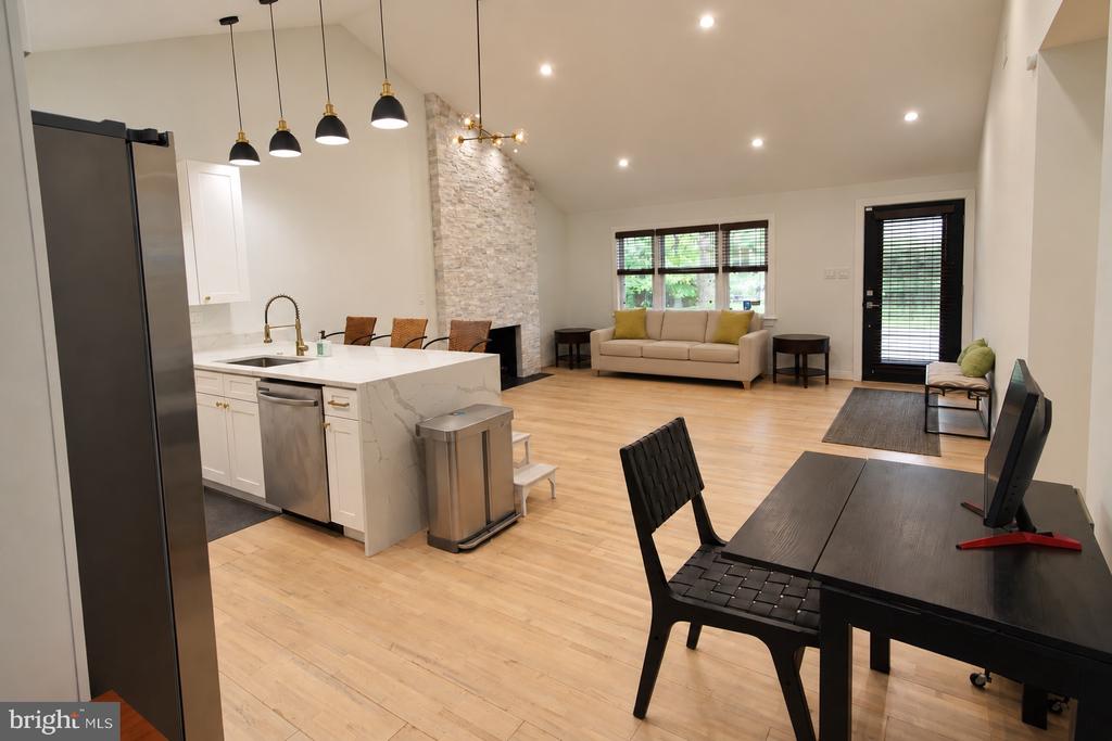 Open-plan kitchen and living room with a stone fireplace, white island, and light wood floors.