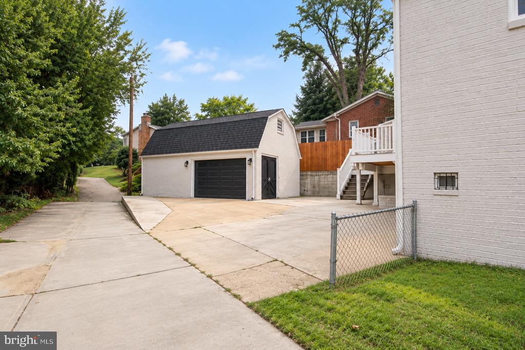 Detached white garage with a black door beside a wide concrete driveway.