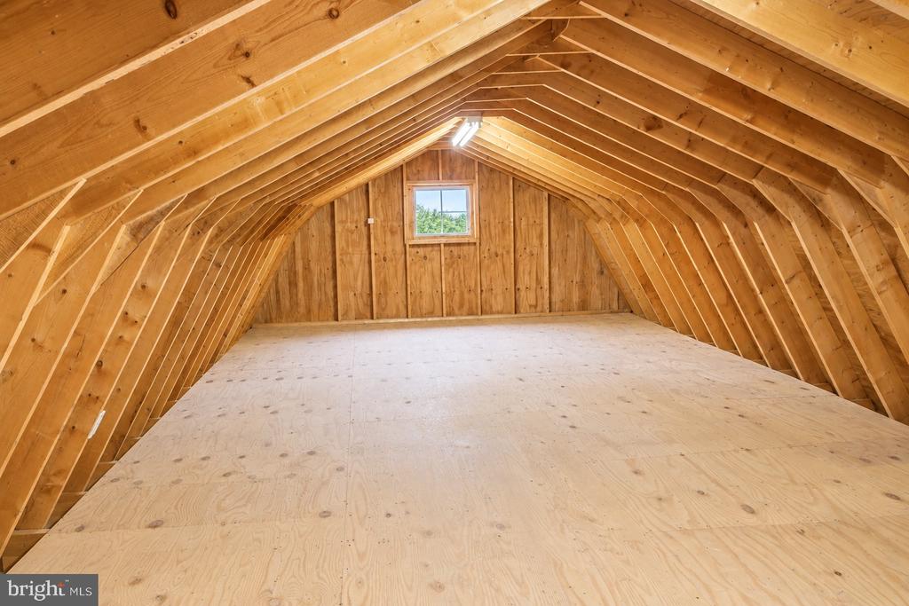 Unfinished attic with exposed timber rafters, plywood flooring, and a small end-wall window.