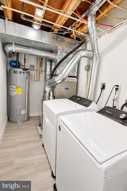 Basement laundry room with white washer and dryer, water heater, and exposed ceiling joists.