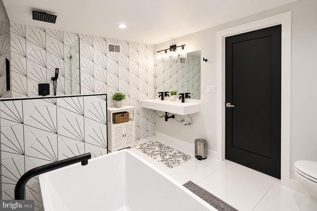 Modern bathroom with a freestanding tub, floating sink, and geometric black-and-white shower tile.