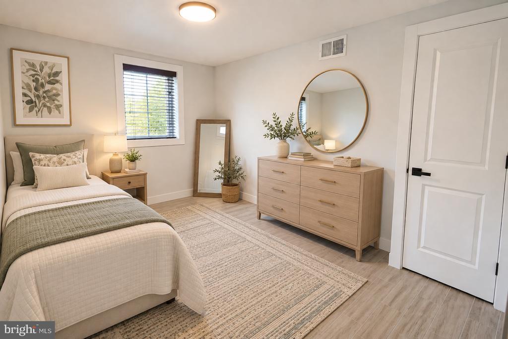 Staged bedroom with neutral bedding, a light wood dresser, and a round mirror.
