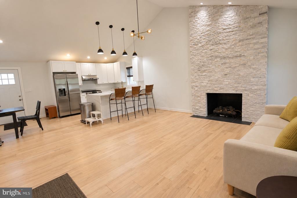 Open-plan kitchen and living room with a stone fireplace, white kitchen, and light hardwood floors.
