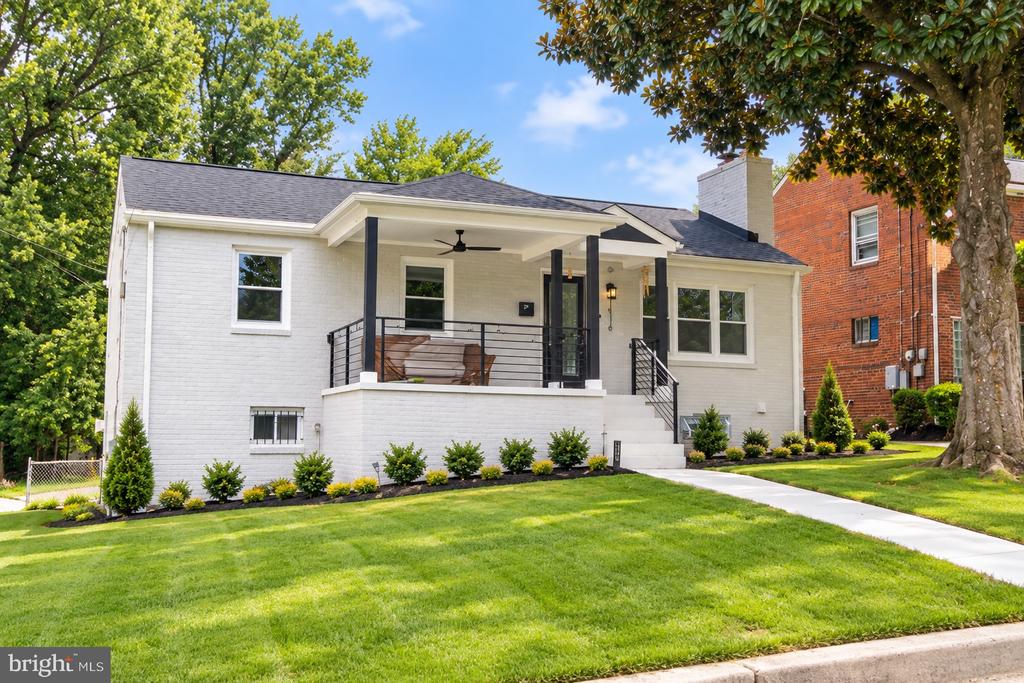 White brick house with a covered front porch, landscaped lawn, and mature shade trees.