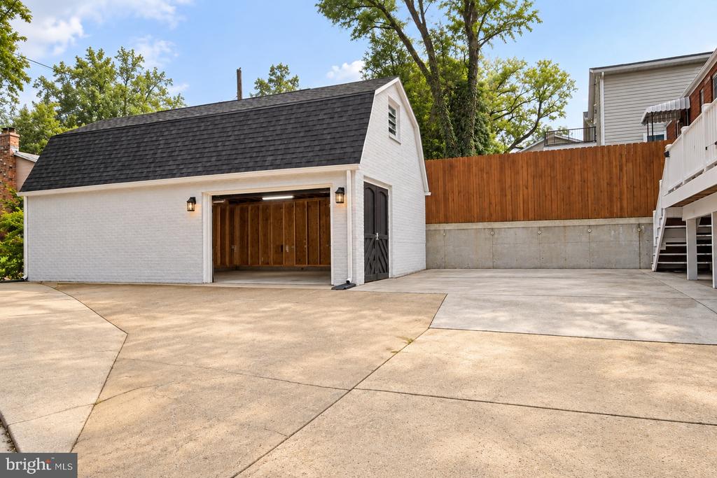 Detached white-brick garage with an open wooden bay beside a broad paved courtyard.