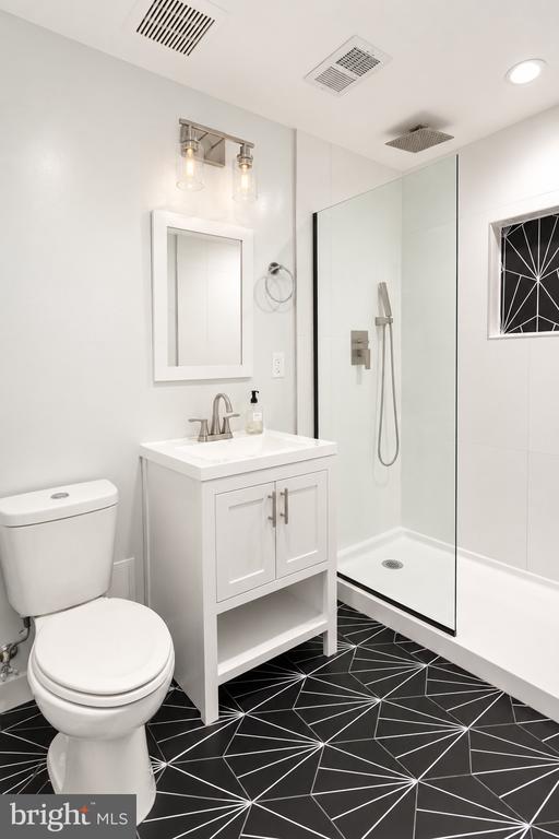 Bathroom with a glass-enclosed shower, white vanity, and black geometric floor tile.