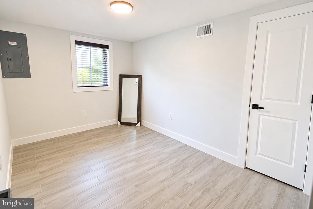 Empty room with light wood-look tile flooring, a window with blinds, and a mirror in the corner.