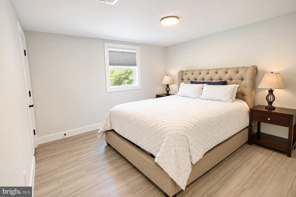 Bedroom with a white-covered bed, tufted tan headboard, and light wood-look flooring.