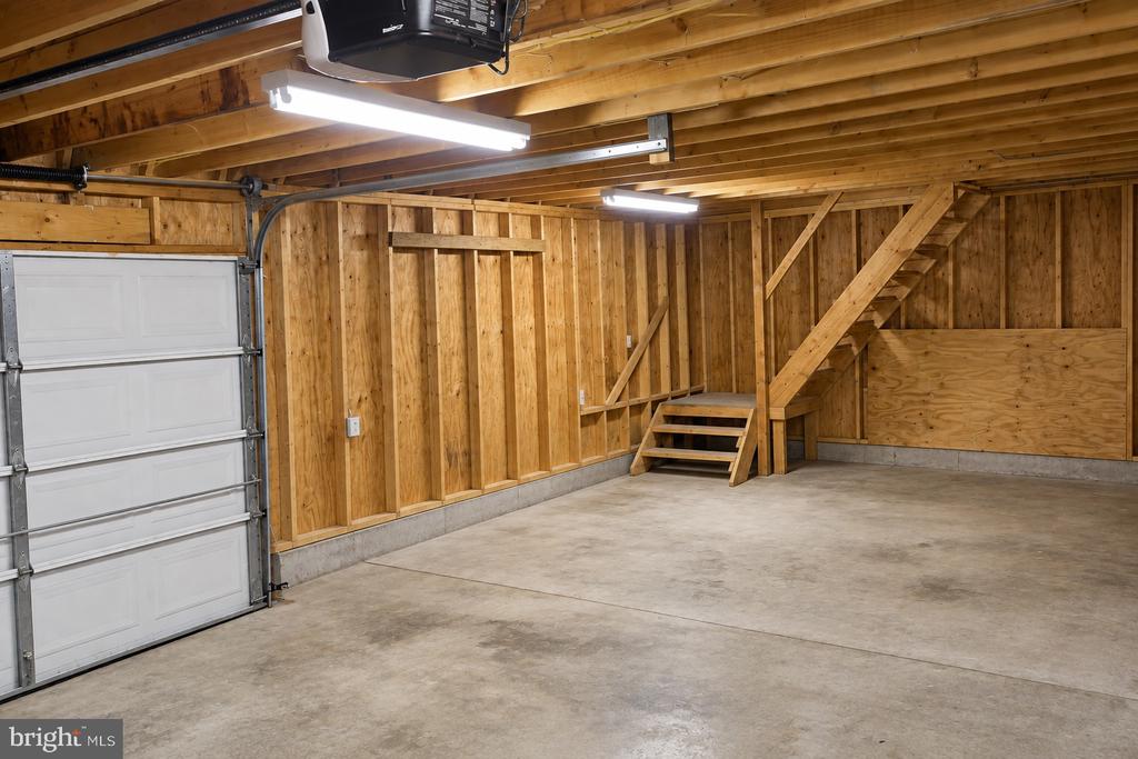 Empty garage with exposed wood framing, concrete floor, and stairs to an upper storage area.