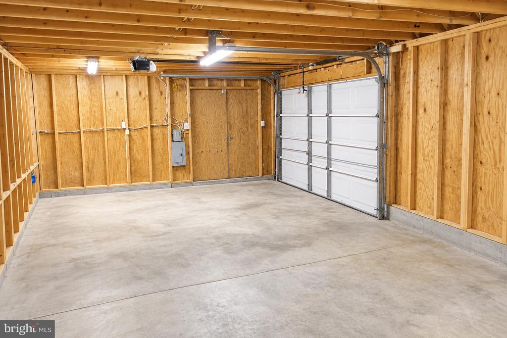 Unfinished garage with exposed wood framing, a concrete floor, and a white sectional door.