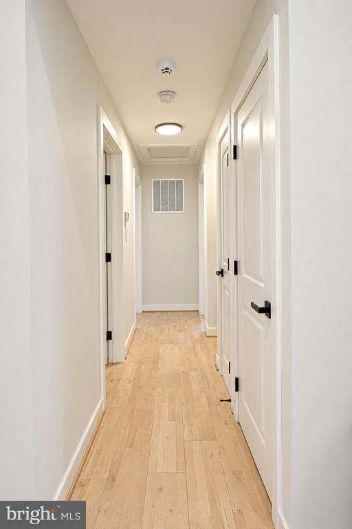 Interior hallway with light wood floors, white paneled doors, and a ceiling light.