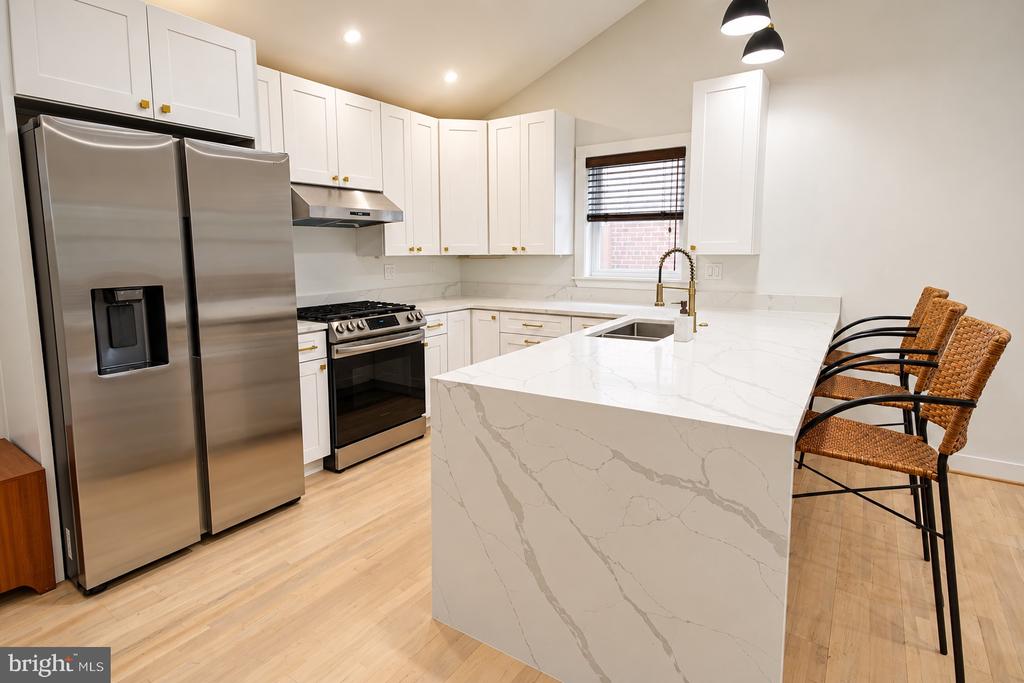 Renovated kitchen with stainless steel appliances, white cabinets, and a large veined quartz island.