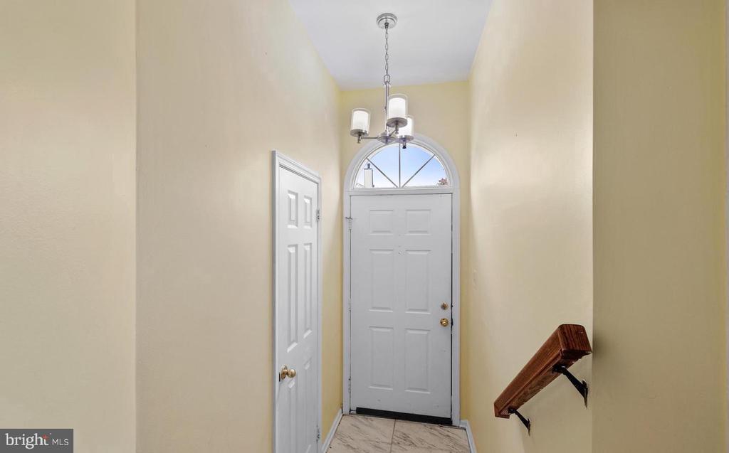 Entry foyer with a white front door, arched transom, chandelier, and marble-look tile.