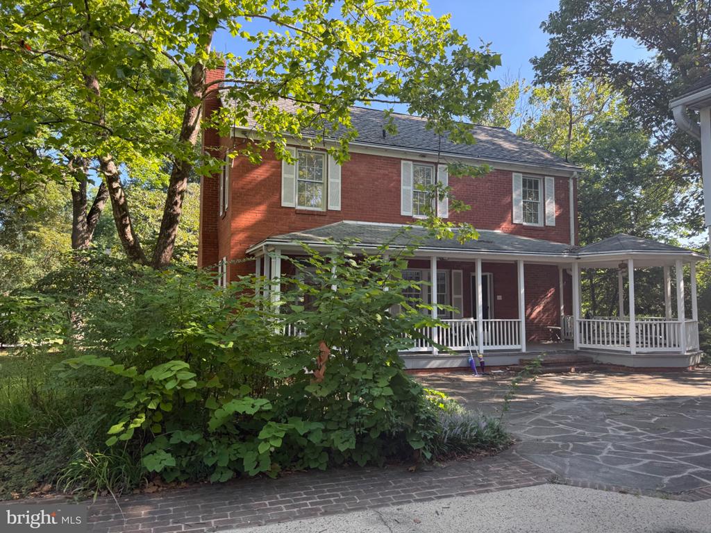 Red-brick house with a white covered porch and gazebo-like extension, framed by mature green trees.