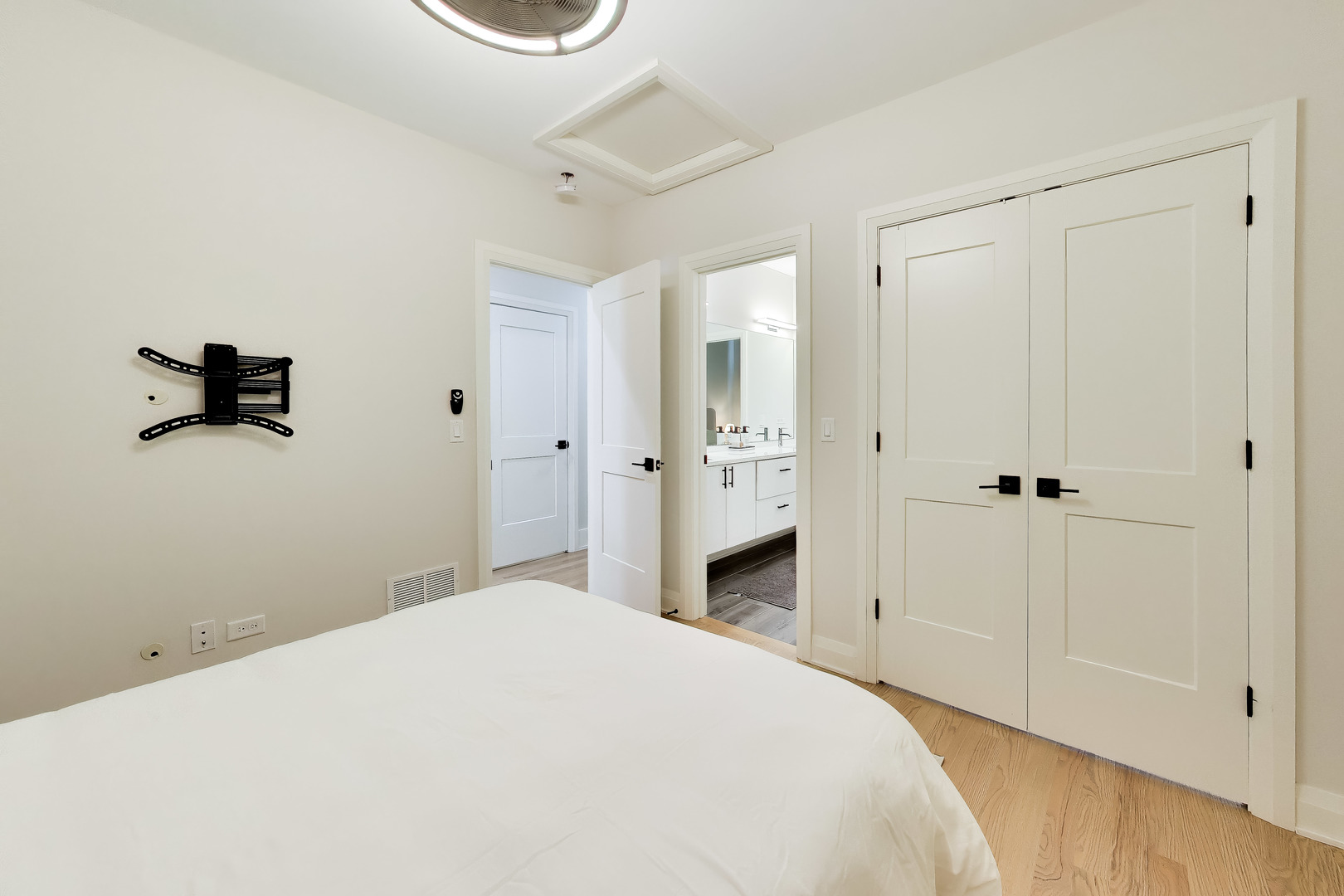 Bedroom with a white bed, wood flooring, and doors opening to an en-suite bathroom.