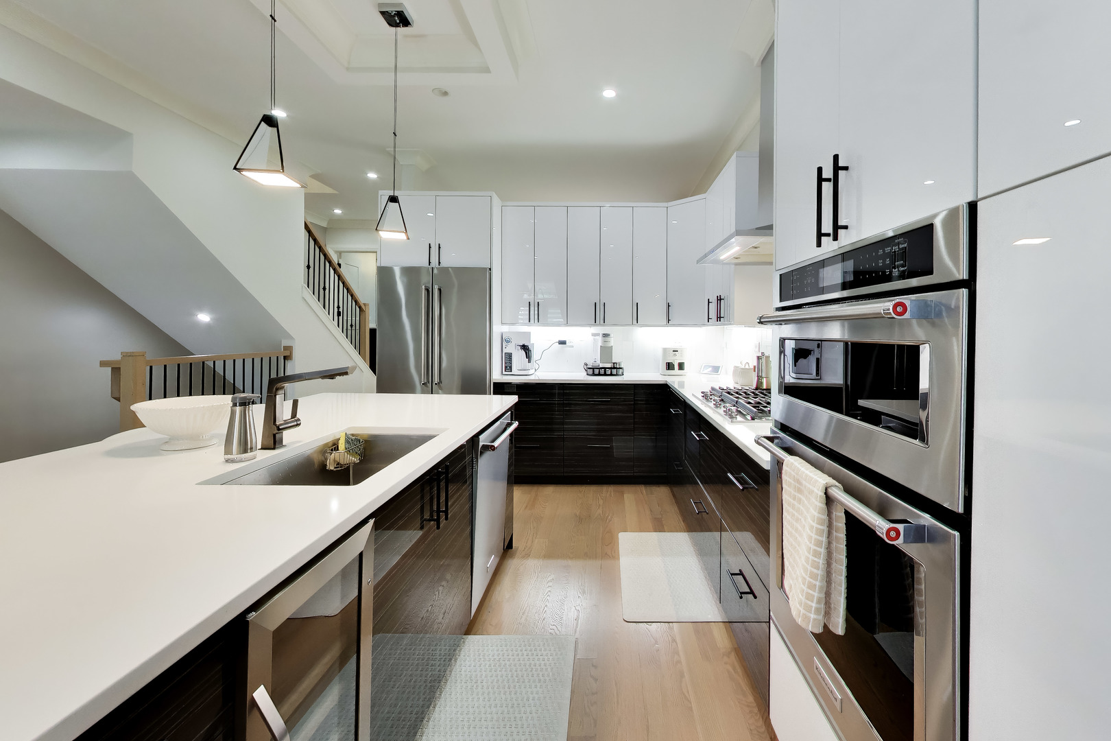 Modern kitchen with white island, dark cabinetry, stainless steel appliances, and pendant lighting.