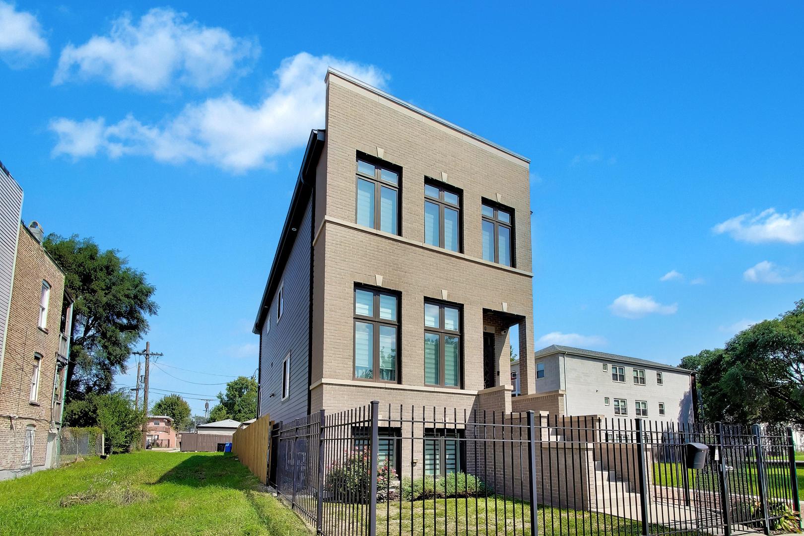 Three-story brick house with tall dark-framed windows and a fenced front yard.