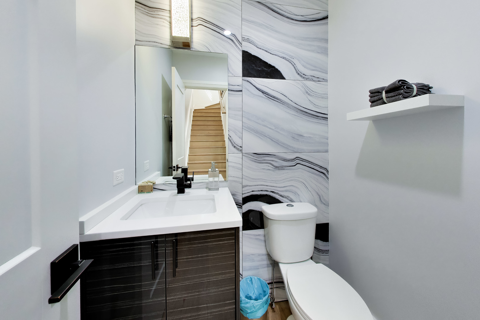 Modern bathroom with a dark wood vanity and gray-veined marble-look wall panels.