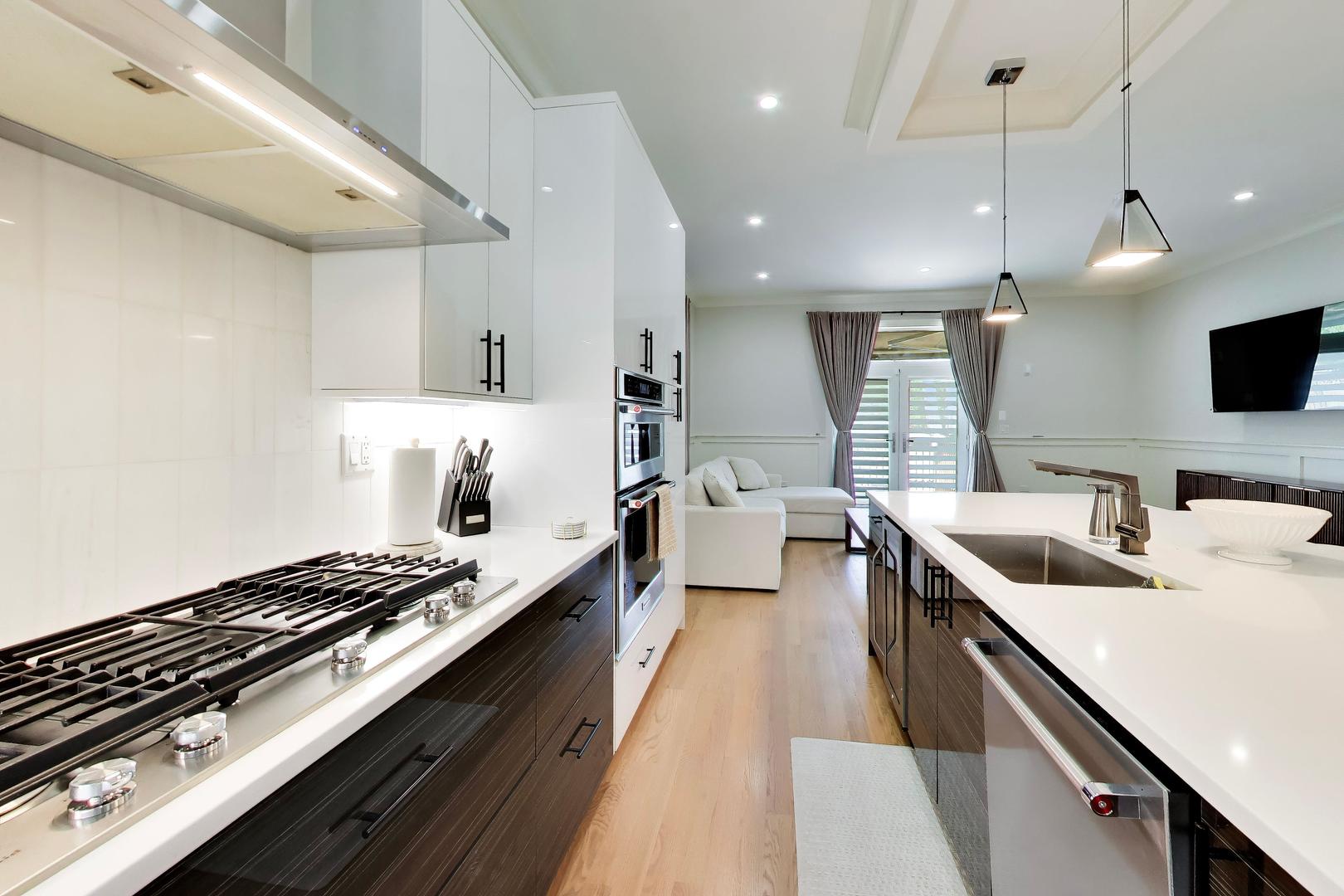 Modern kitchen with a white island, gas cooktop, built-in ovens, and an adjoining living area.
