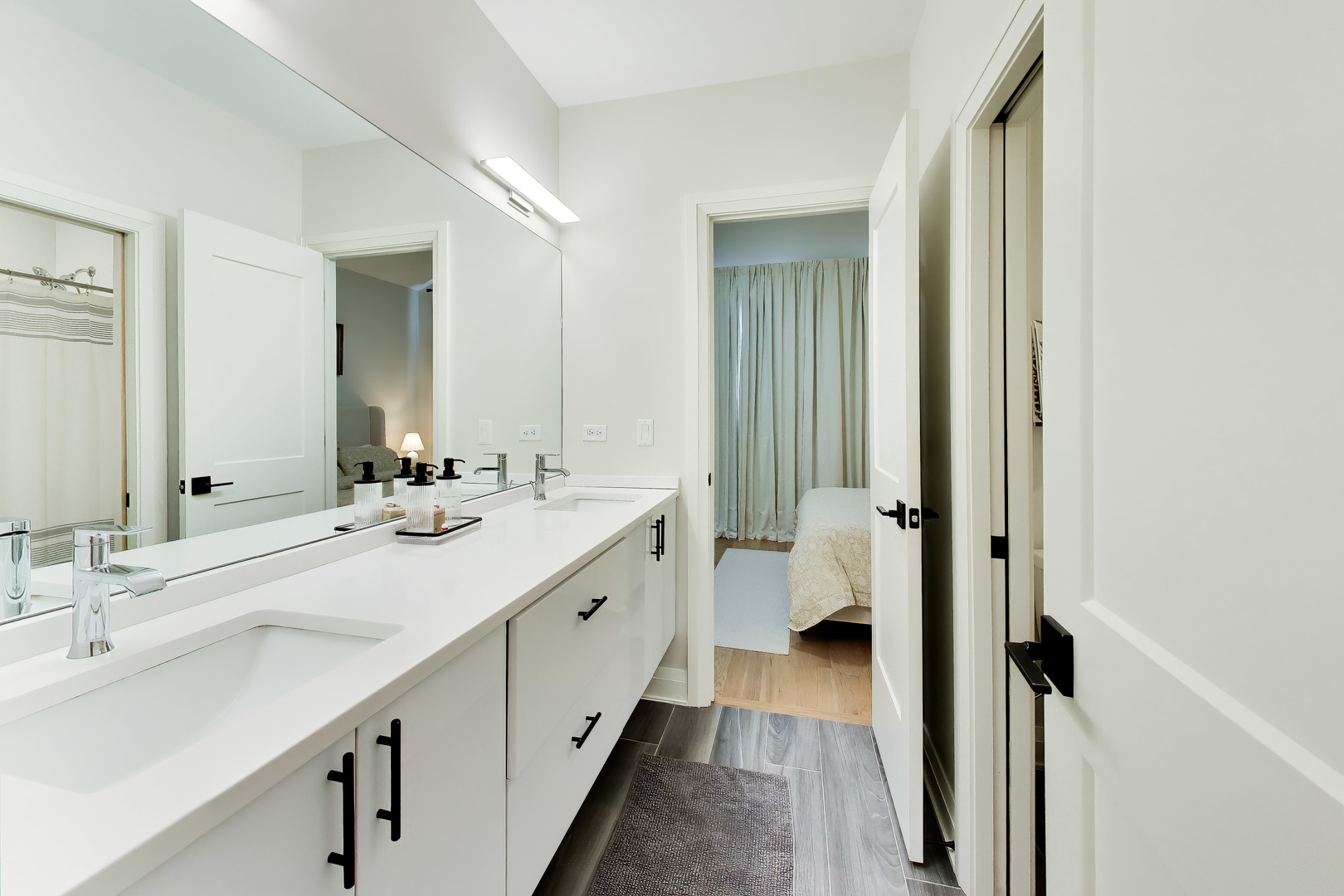 Bathroom with long white vanity, mirrored wall, and open doorway to a bedroom.