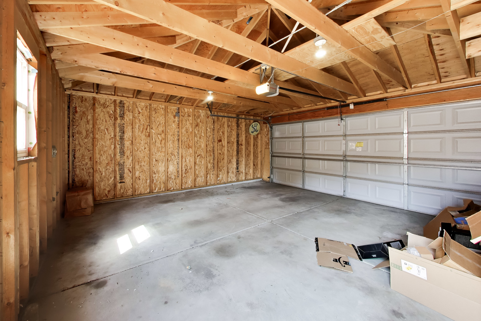 Garage with exposed wood framing, concrete floor, and white overhead door.
