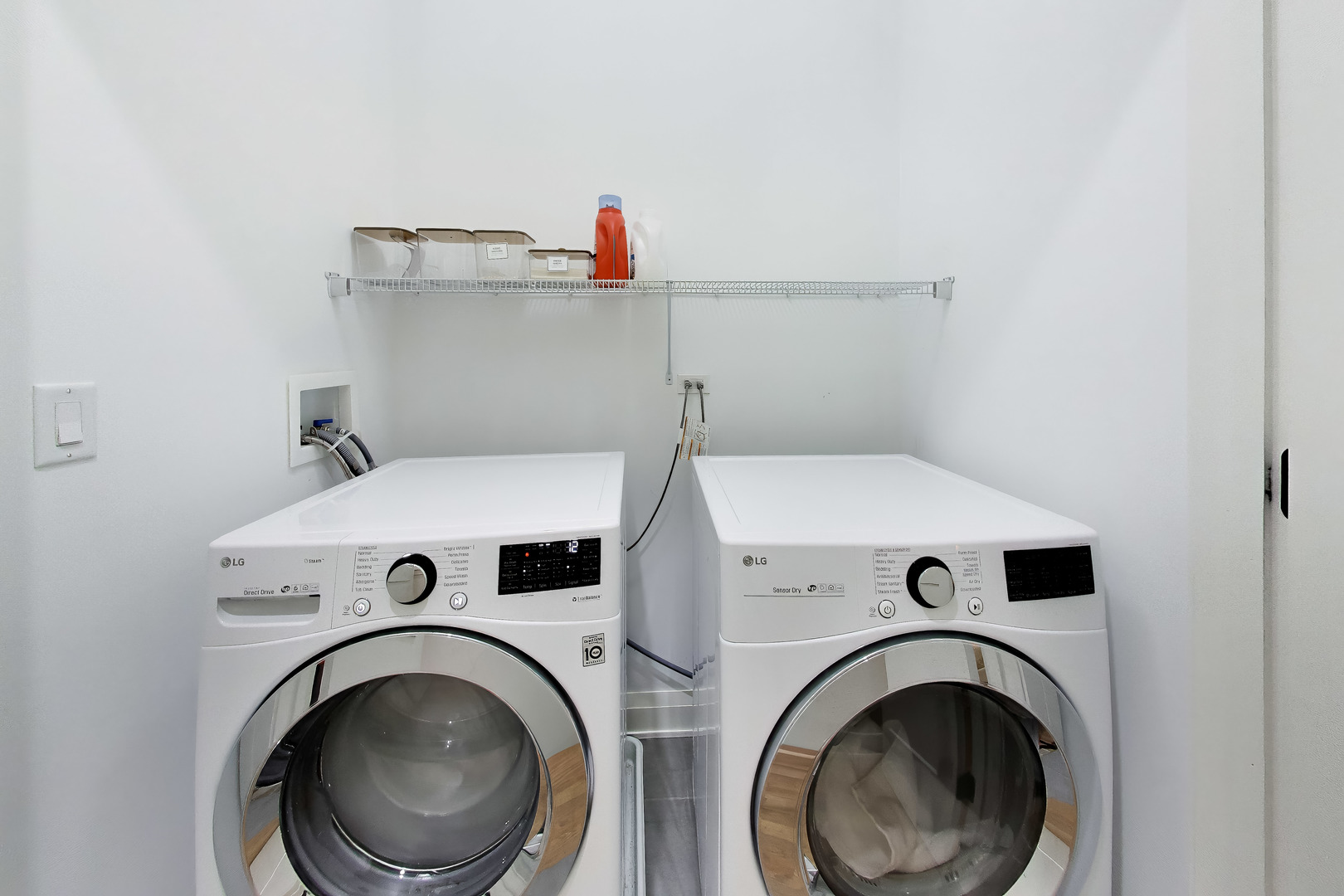 Laundry room with side-by-side white front-loading washer and dryer beneath a wire shelf.