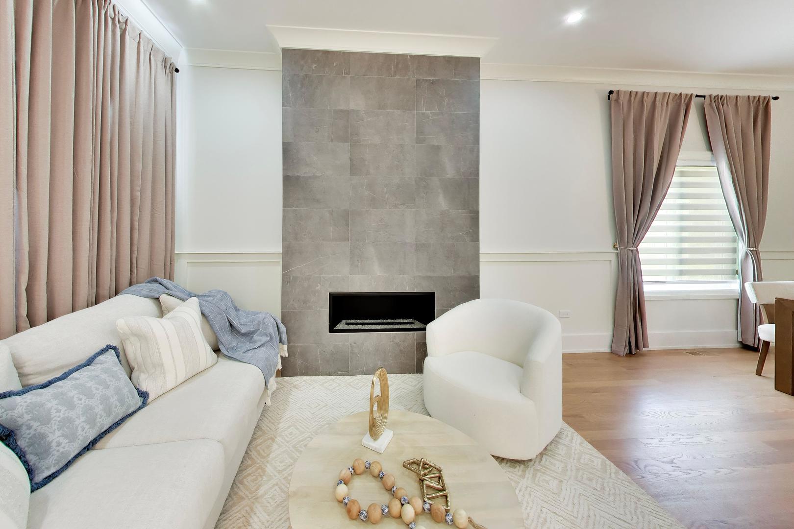 Staged living room with a gray tiled fireplace and cream seating.