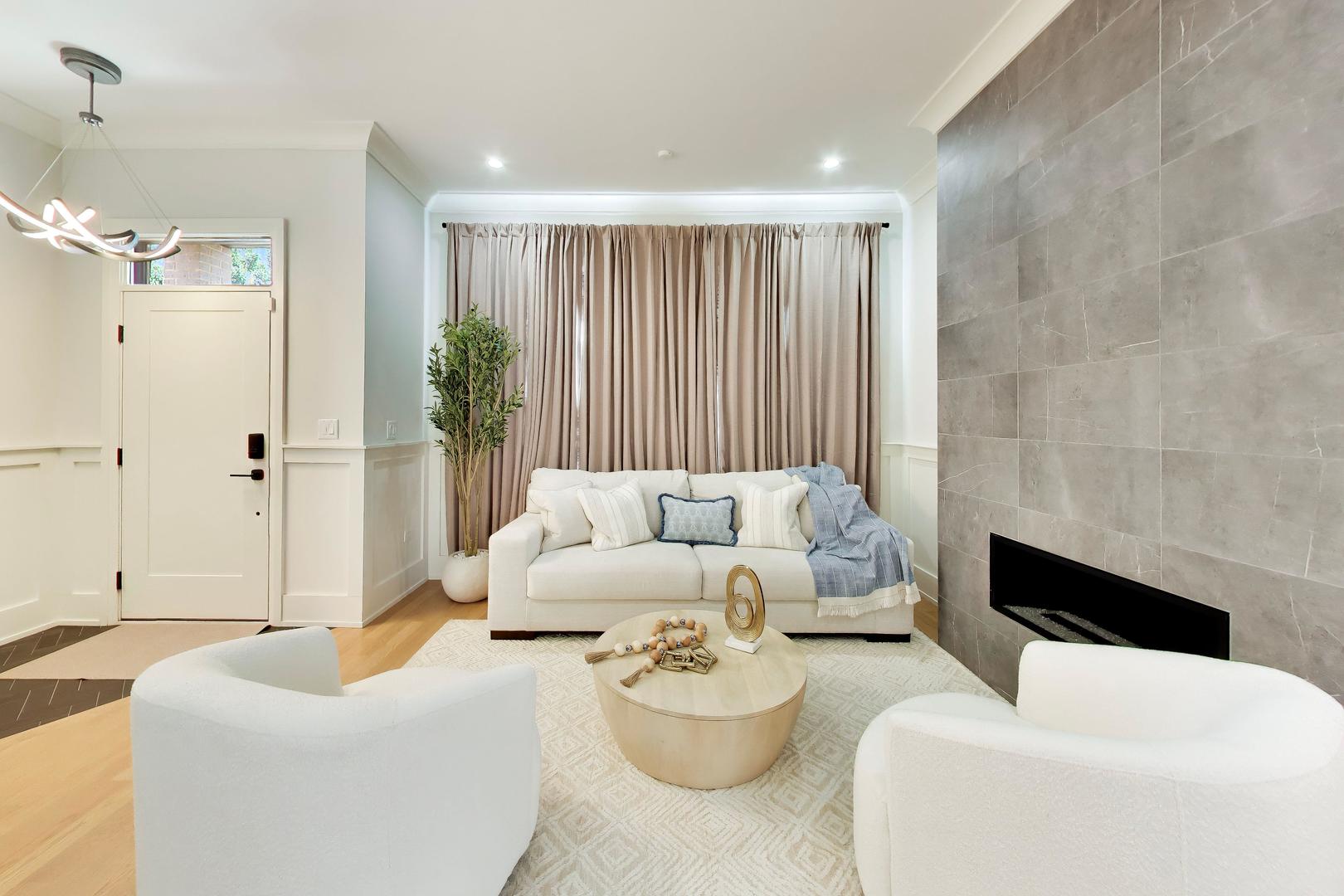 Staged living room with white seating, a round coffee table, and a large gray tiled fireplace.