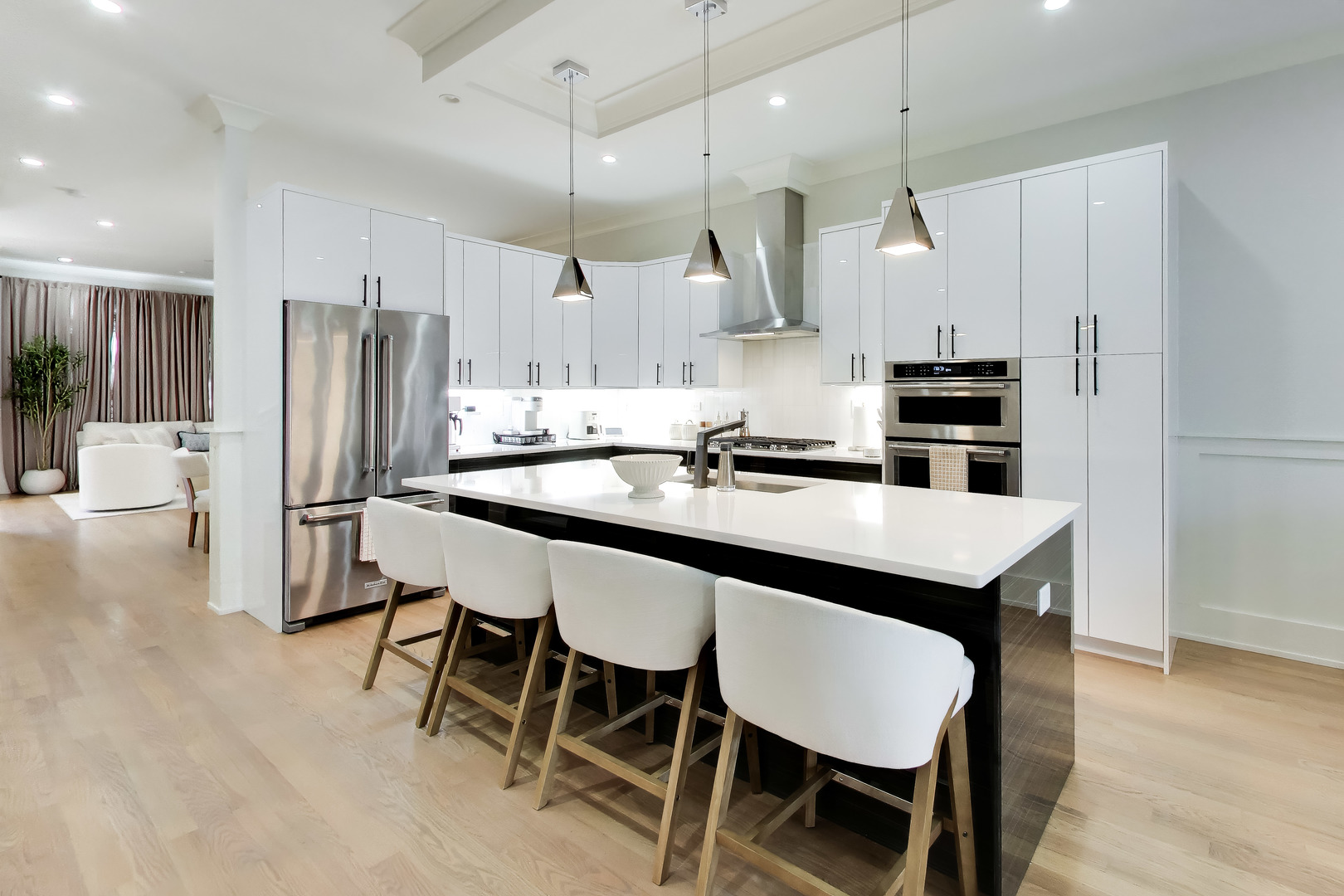Modern kitchen with a large island, white cabinetry, stainless steel appliances, and pendant lights.