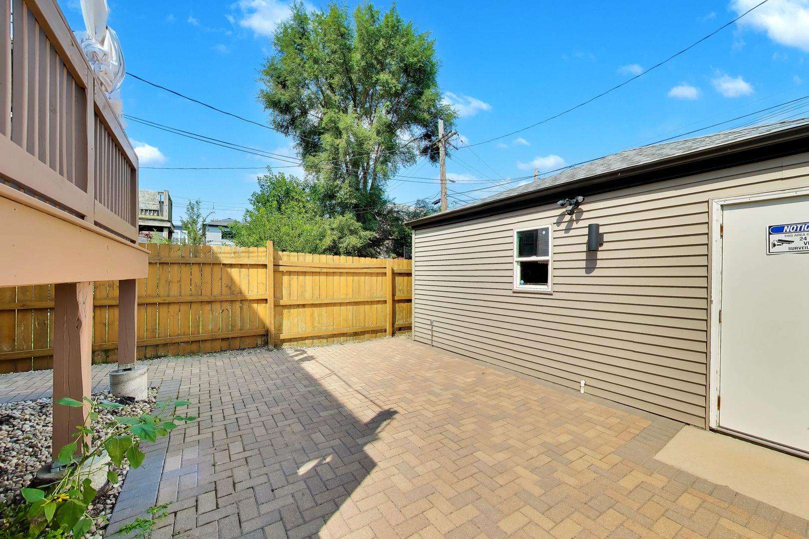 Backyard patio with brick pavers, a wooden privacy fence, and a beige-sided outbuilding.