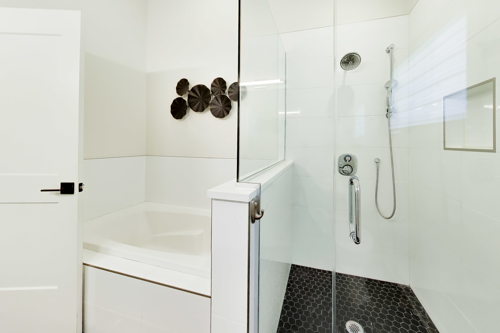 Modern bathroom with a white tub beside a glass shower with black hexagonal floor tiles.