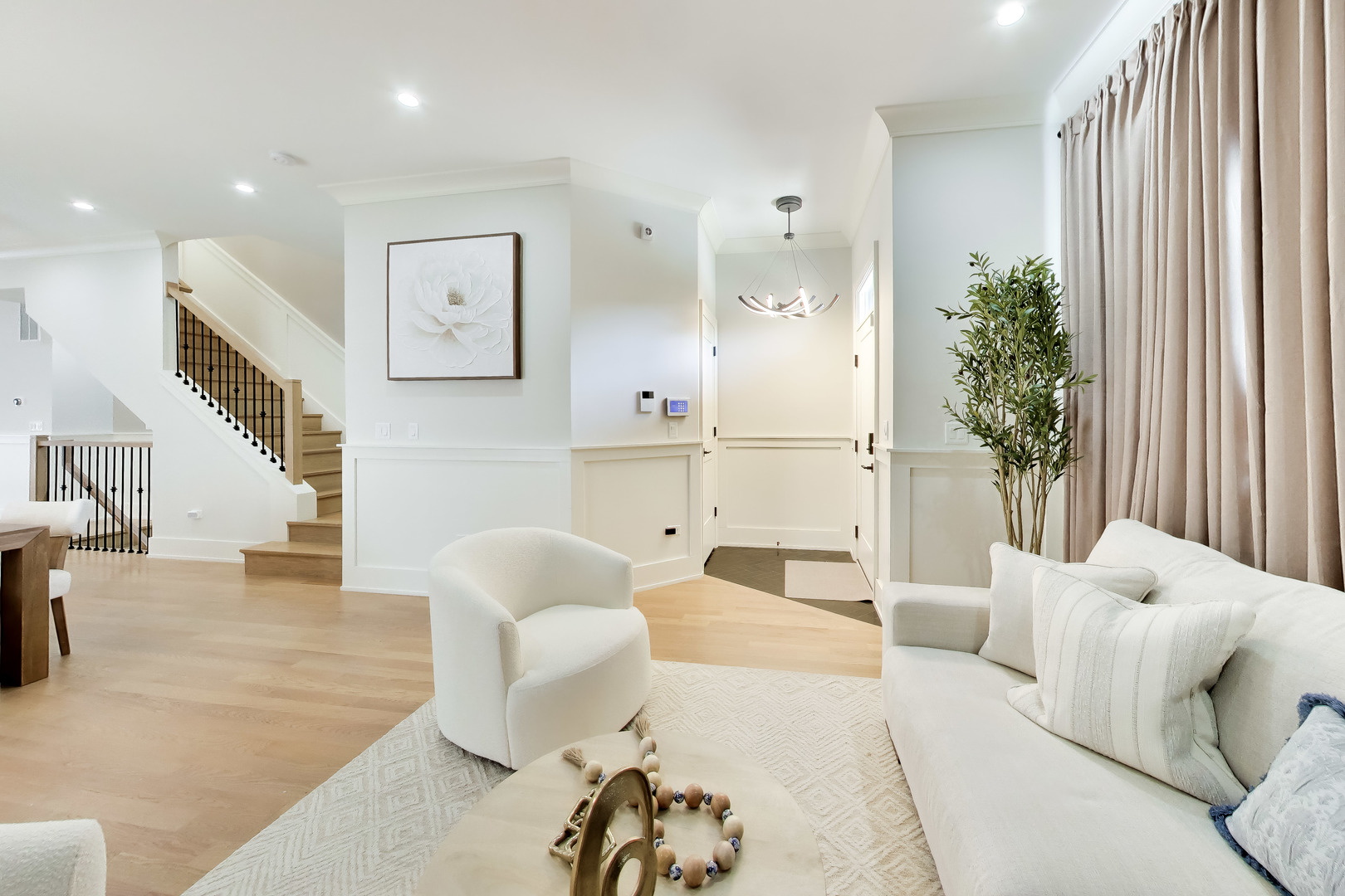 Living room with white seating, pale wood floors, and a staircase with black balusters.