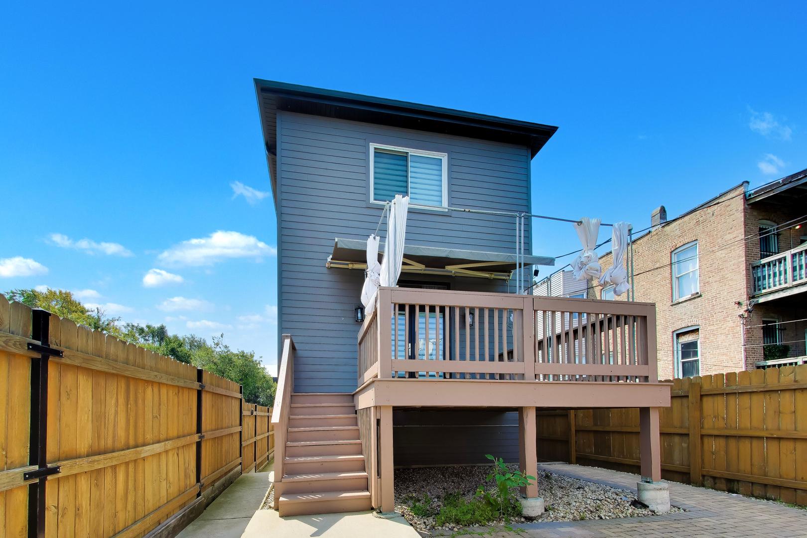 Rear of a gray two-story home with a raised deck, stairs, and fenced yard.
