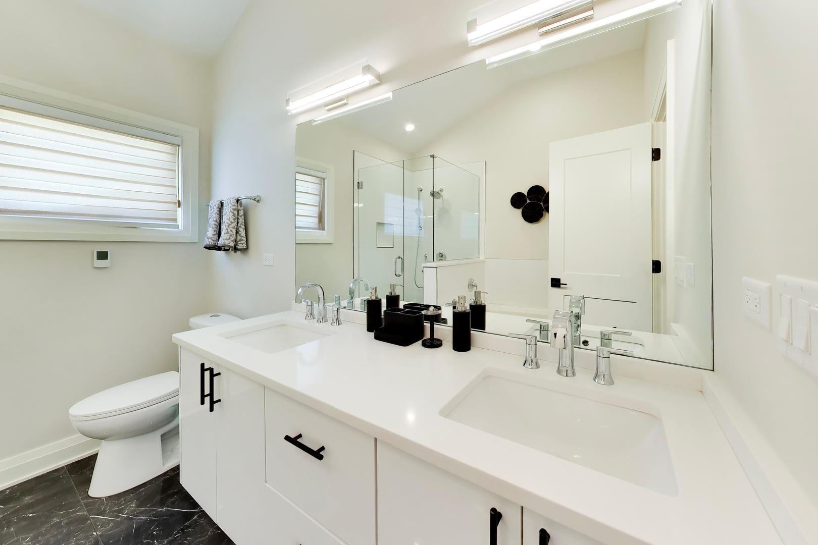 Modern bathroom with a double-sink vanity, glass shower, and dark tile floor.