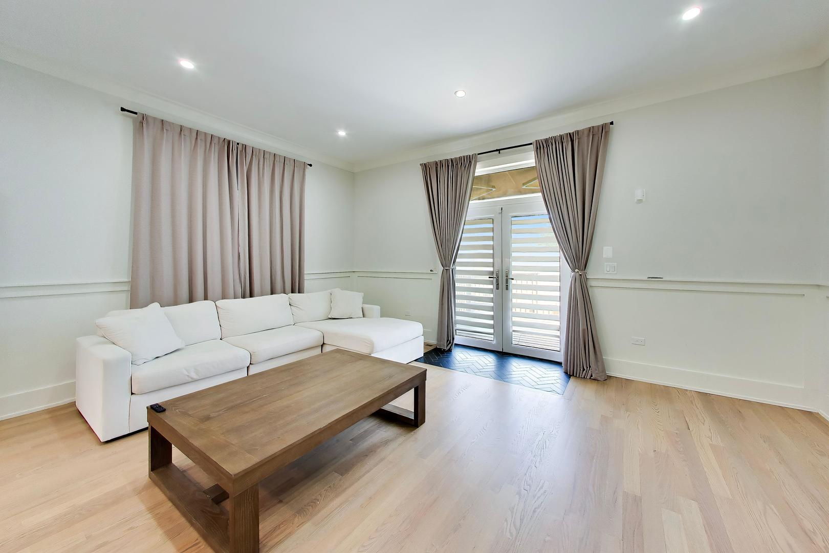 Living room with a white sectional sofa, wood coffee table, and curtained glass doors.