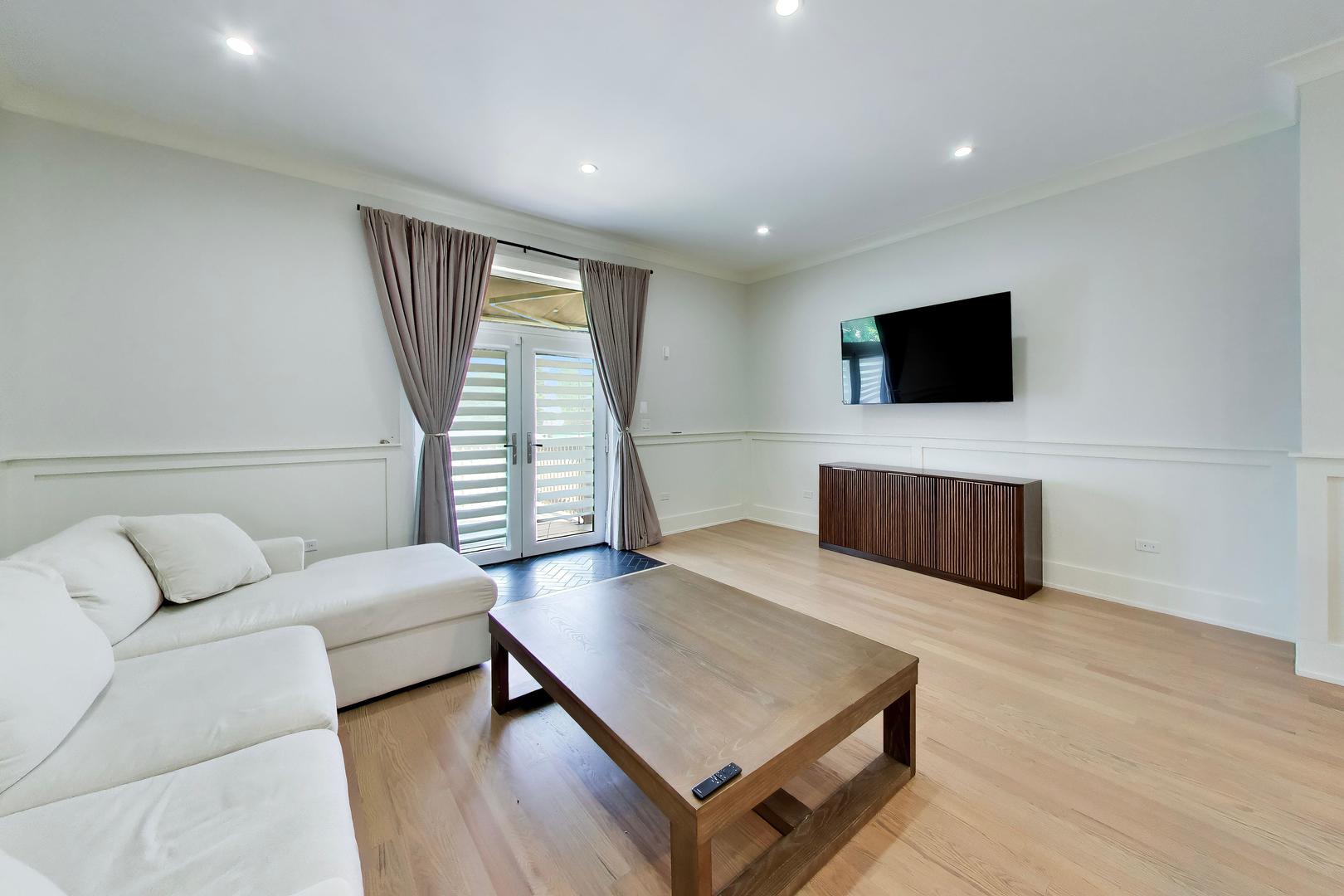 Living room with a white sectional, wooden coffee table, and French doors with striped shades.