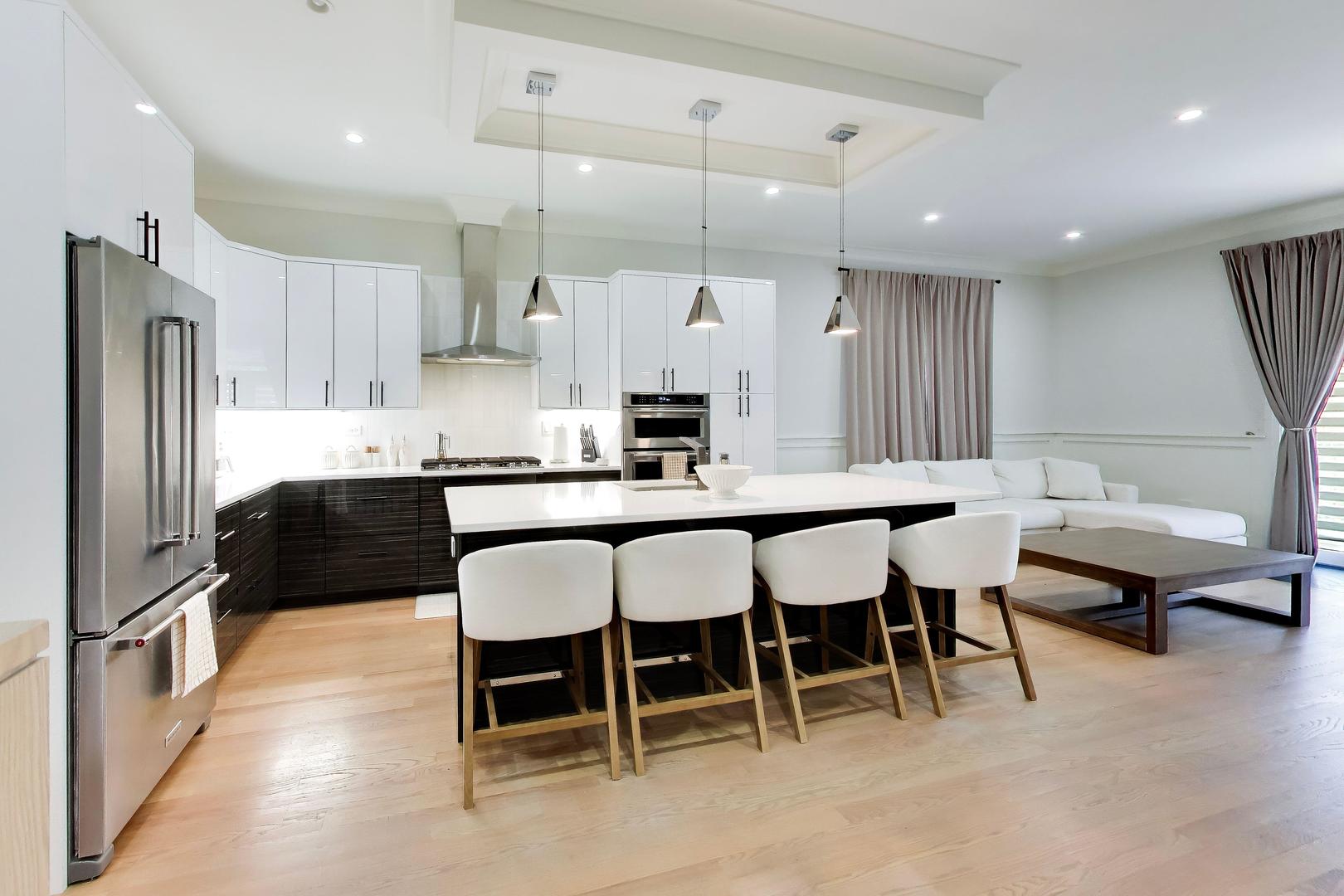 Open-plan kitchen with a large island and four stools beside a white sectional sofa.