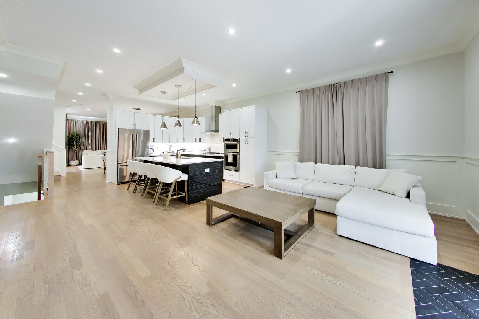 Open-plan living room and kitchen with a white sectional, pale wood floors, and a black island with bar seating.