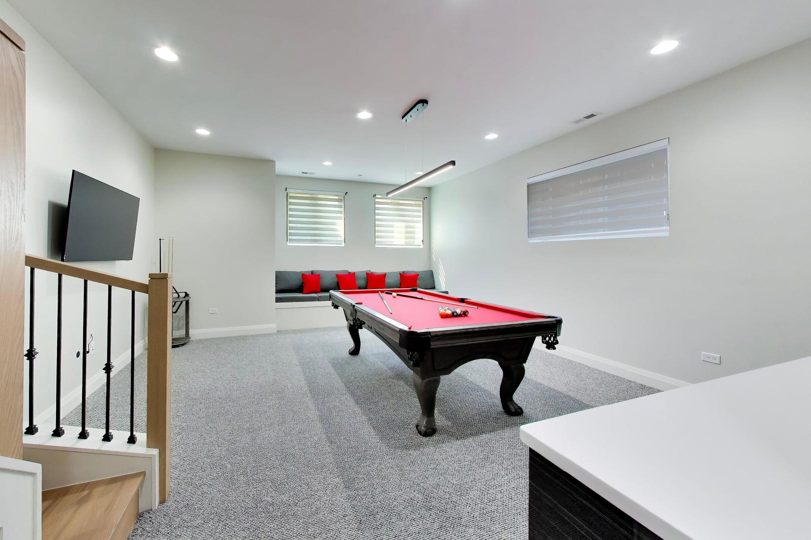 Basement game room with a red pool table, built-in seating, and a wall-mounted television.