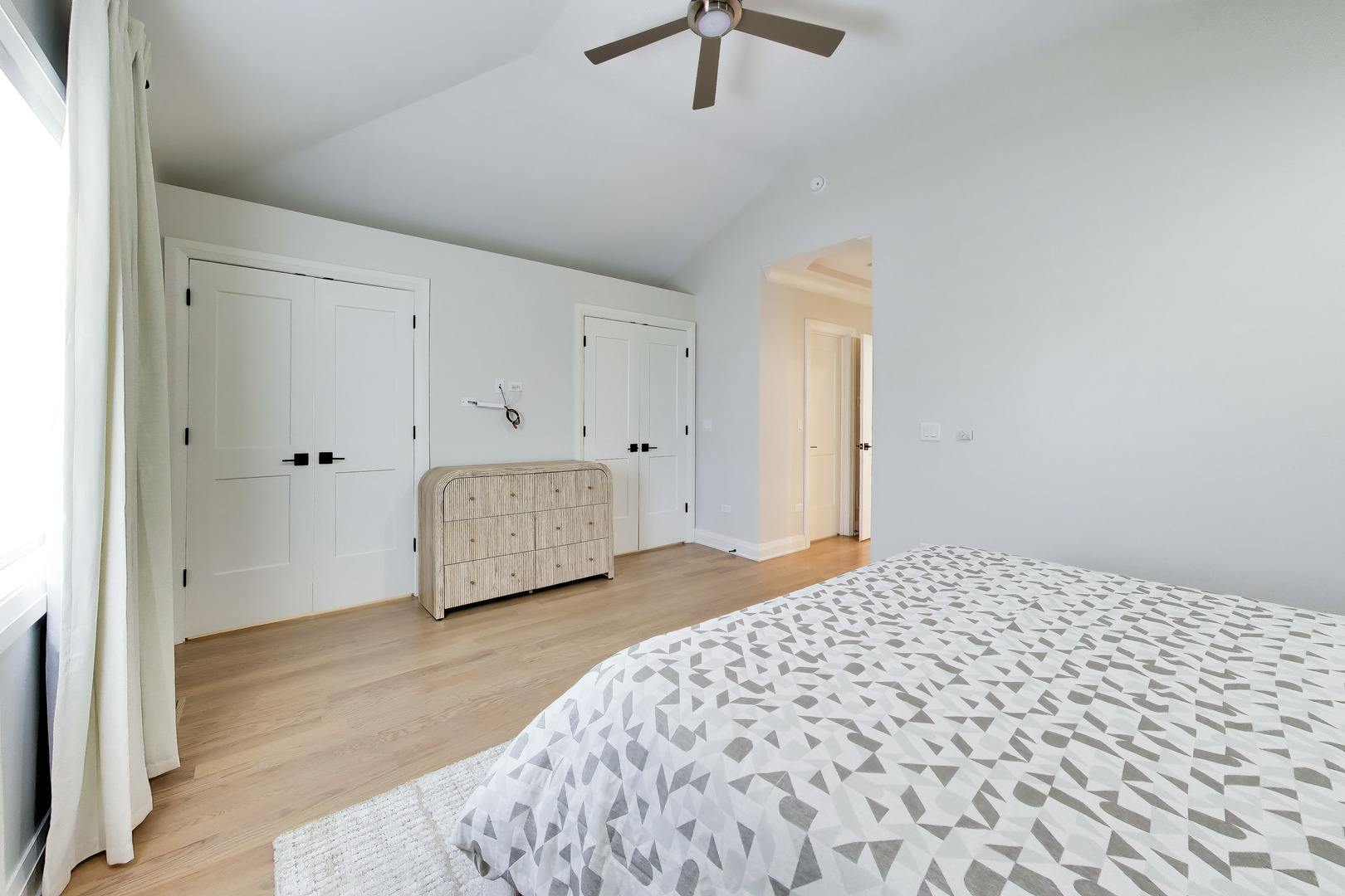 Bedroom with a geometric-patterned bedspread, vaulted ceiling, and ceiling fan.